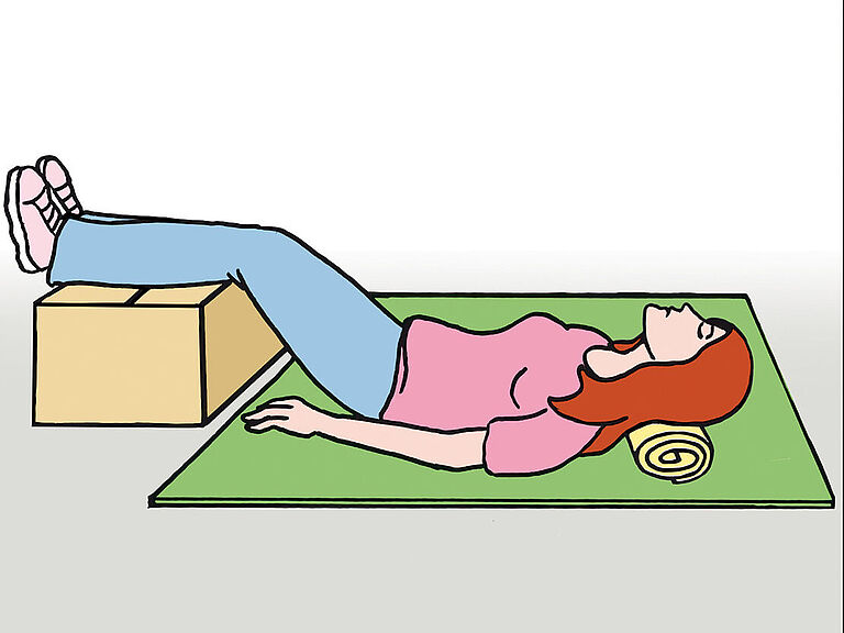 Hitzeerschöpfung: Eine Frau liegt flach am Boden mit erhöhten Beinen auf einer Kiste sowie leicht erhöhtem Kopf auf einer Handtuchrolle.