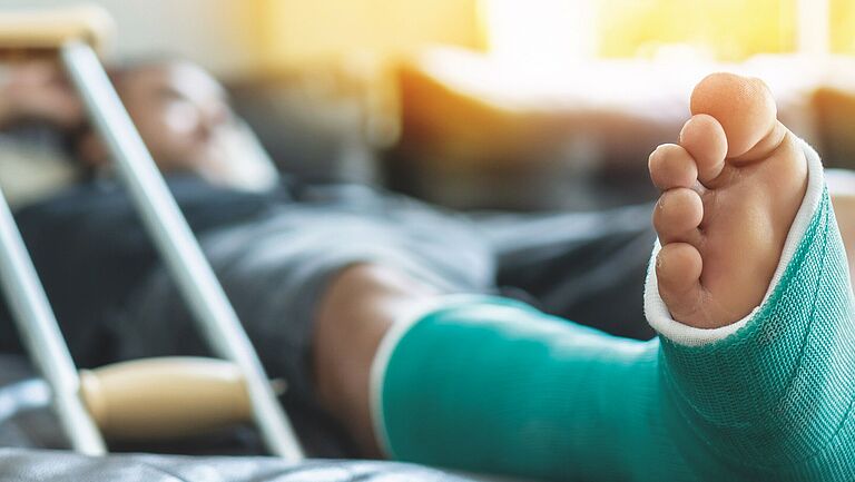 Eingegipster Fuß mit Gehhilfe im Hintergrund