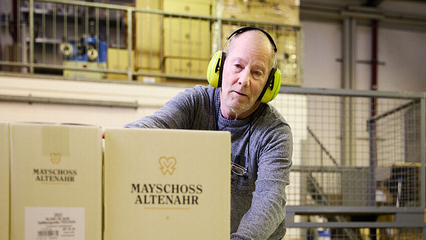 Hans-Joachim Raths, Aushilfsmitarbeiter der Winzergenossenschaft, verlädt Kartons und trägt dabei Gehörschutz. 