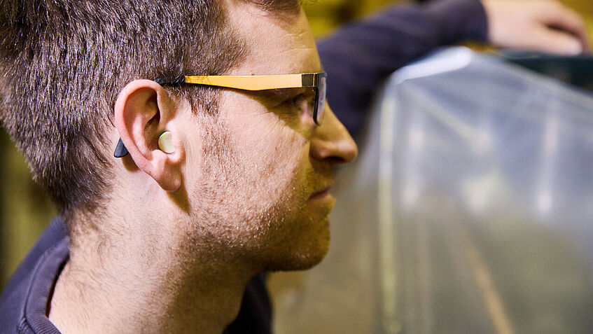 Ein Beschäftigter der Winzergenossenschaft ist im Seitenprofil fotografiert. Er trägt im rechten Ohr einen Gehörschutzstöpsel. 