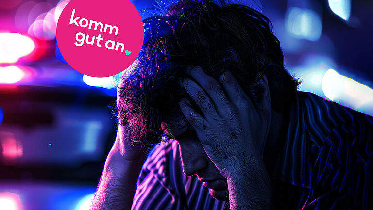 Verzweifelter junger Mann sitzt nachts am Straßenrand vor einem Polizeiwagen mit blau-roten Einsatzlichtern und hält den Kopf in den Händen. Im Bild befindet sich ein pinker Kreis mit dem Slogan ‚komm gut an‘. Symbolfoto für Unfall, Notfall, Stress im Straßenverkehr und Verkehrssicherheit.