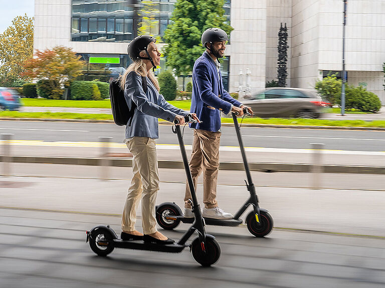 E-Scooter im Straßenverkehr Eine Frau und ein Mann fahren jeweils einen E-Scooter parallel zueinander.