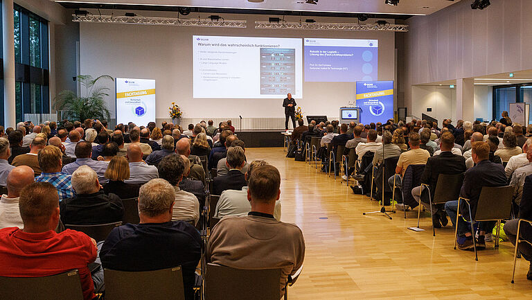 Eröffnung der BGHW-Fachtagung 2024 - Blick über vollbesetzte Stuhlreihen aufs Podium