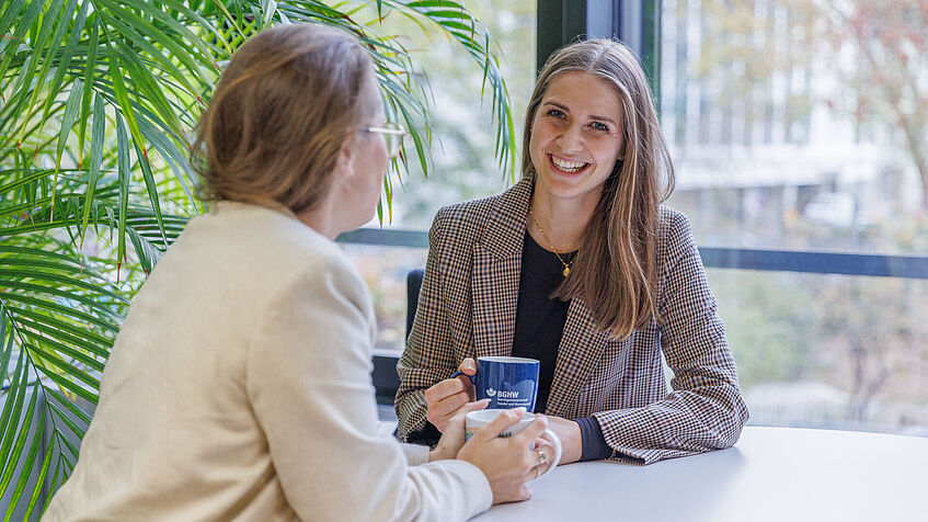 Zwei Frauen unterhalten sich und sitzen dabei an einem Tisch.