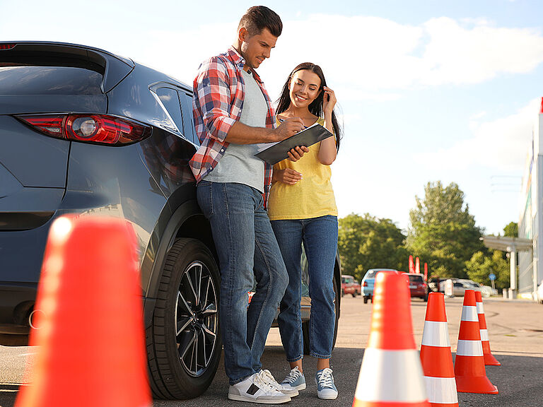 PKW Sicherheitstraining. Fahrlehrer und Schülerin stehen am Auto und schauen auf Notizen.